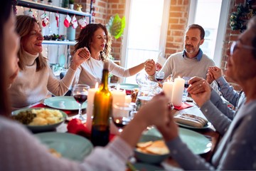 Family and friends dining at home celebrating christmas eve with traditional food and decoration, praying and blessing the table