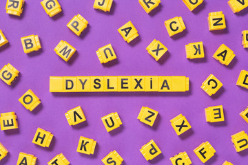 Dyslexia word yellow on pink purple with scattered letters cubes around, reading difficulty and...