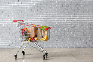 Shopping cart with products near brick wall