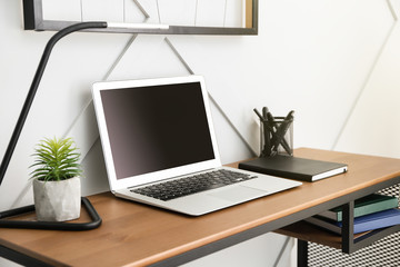 Comfortable workplace with modern laptop near light wall