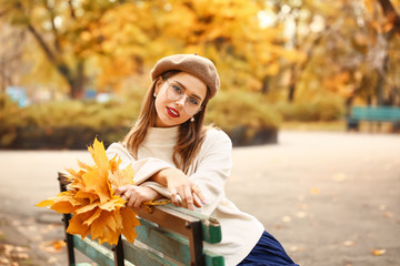 Stylish young woman sitting on bench in autumn park