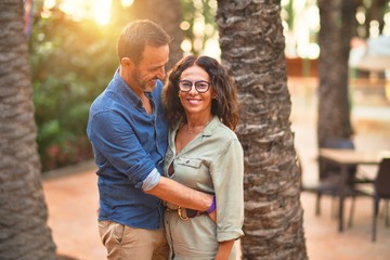 Naklejka premium Middle age beautiful couple smiling happy and confident at town park. Standing with smile on face and hugging