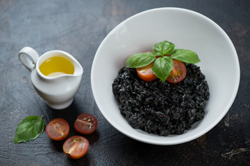 Risotto with squid-ink served in a white bowl over dark brown stone surface, studio shot