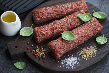 Raw fresh kebabs made of marbled beef meat and seasonings on a wooden cutting board, studio shot
