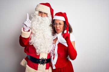 Middle age couple wearing Santa costume hugging over isolated white background Pointing up looking sad and upset, indicating direction with fingers, unhappy and depressed.