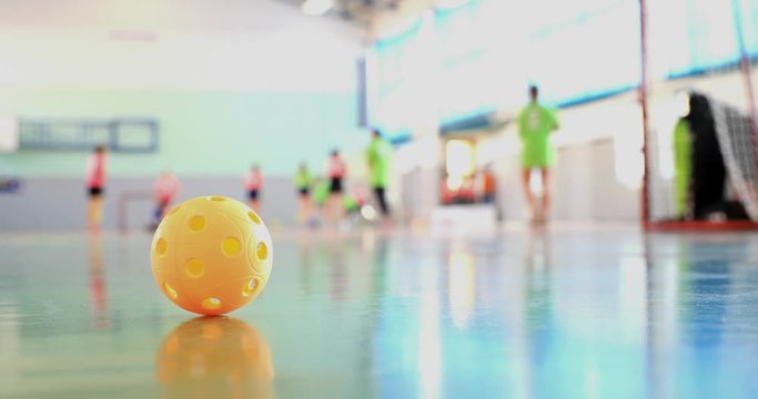 Floorball match of small floorball players. Children play floorball match in indoor hall. Intentionally focused on the ball in the foreground. Players in the background intentionally out of focus.
