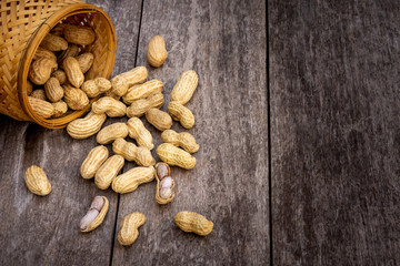 Peeled and unpeeled peanut or goober  in wooden basket and spilling out on the rustic wood table. Healthy food concept. Top view.