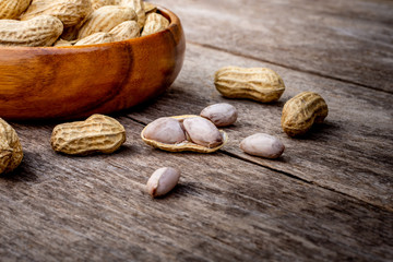 Peeled and unpeeled peanut or goober  in wooden bowl and spilling out on the rustic wood table. Healthy food concept.