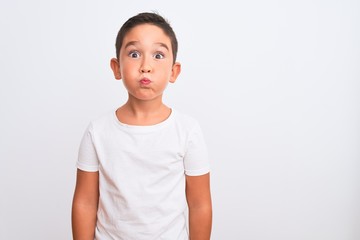 Beautiful kid boy wearing casual t-shirt standing over isolated white background puffing cheeks with funny face. Mouth inflated with air, crazy expression.