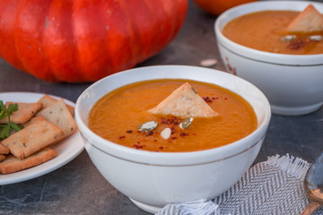 Vegetarian autumn pumpkin cream soup decorated crackers and pumpkin seedswith in white bowls, close up. Autumn and winter vegetarian food concept. 