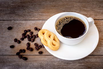 Mockup hot black coffee in white porcelain cup with cookie and coffee beans isolated on rustic wood table background. Healthy drinks and lifestyle concept. Vintage dark tone. 