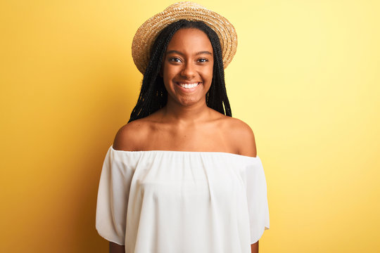 Young african american woman wearing white t-shirt and hat over isolated yellow background with a happy and cool smile on face. Lucky person.