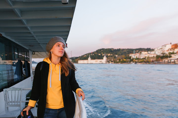 Woman in a yellow sweater and gray beret standing on deck of cruise ship and looking at landscape....