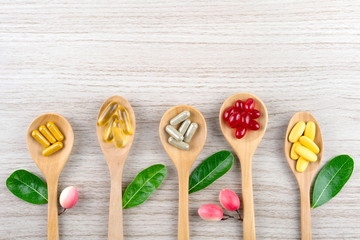 Alternative herbal medicine, vitamin and supplements from natural, pills and capsules in spoon on wood table, drug concept