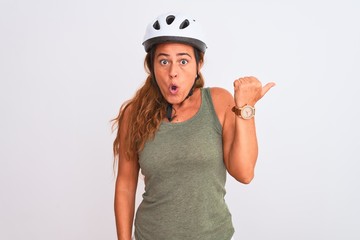 Middle age mature cyclist woman wearing safety helmet over isolated background Surprised pointing with hand finger to the side, open mouth amazed expression.