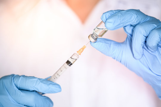 Nurse or doctor hand in blue glove holding flu, measles vaccine vial and syringe wiht needle for pregnant women vaccination, medicine and drug concept