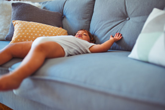 Beautiful toddler child girl wearing white bodysuit lying down on the sofa