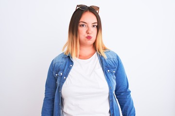 Beautiful woman wearing denim shirt standing over isolated white background puffing cheeks with...