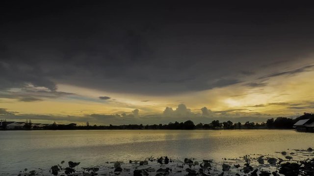 Timelapse evening of dark clouds moving above the lake with sunset and yellow sun light in cloudy sky background, Krajub reservoir, Nonk Kop in Ban Pong District, Ratchaburi, Thailand.