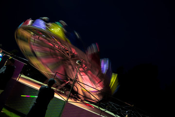 Amusement park ride fast spinning carousel roundabout with motion blur. Fun fair carnival  rides at fairground. Family vacation, leisure and recreation concept