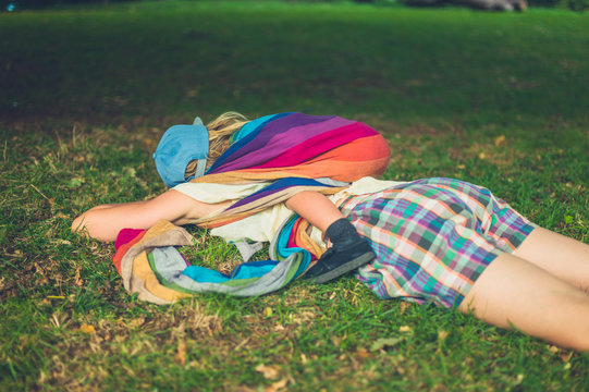 Young mother lying in grass with sleeping toddler on her back