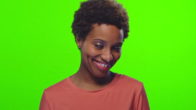 Portrait of playful funny young African American woman with glad expression, blinks eye, flirts with boyfriend, expresses good emotions, over chroma key background. Hey, guy look at me