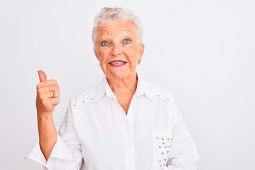 Senior grey-haired woman wearing elegant shirt standing over isolated white background smiling with happy face looking and pointing to the side with thumb up.