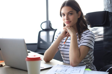 Beautiful young woman is sitting in the office and looking at camera. © ty