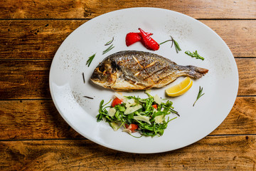 Grilled fish with arugula salad on white plate. Top view landscape image