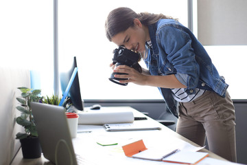 Concentrated young designer using digital camera while standing near the desk in her creative office.