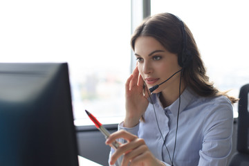Beautiful smiling call center worker in headphones is working at modern office