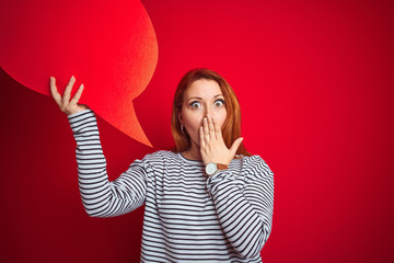 Young beautiful redhead woman holding speech bubble over red isolated background cover mouth with...