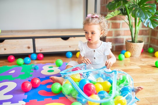 Beautiful caucasian infant playing with toys at colorful playroom. Happy and playful wth colorful balls at kindergarten.