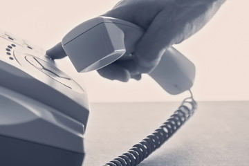 Closeup of male hand holding telephone receiver and dialing a phone number on a classical landline...