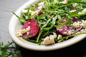 Clay dish with beetroot arugula and feta cheese salad on slate stone tray closeup view