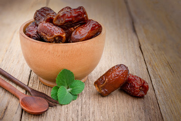 Closeup date palm fruits in wooden bowl isolated on wood table background. 