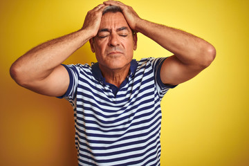 Handsome middle age man wearing striped polo standing over isolated yellow background suffering from headache desperate and stressed because pain and migraine. Hands on head.