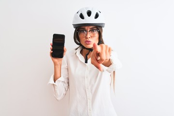 Young businesswoman wearing bike helmet holding smartphone over isolated white background pointing with finger to the camera and to you, hand sign, positive and confident gesture from the front