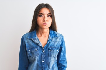 Young beautiful woman wearing casual denim shirt standing over isolated white background puffing cheeks with funny face. Mouth inflated with air, crazy expression.