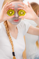 Happy young woman having face mask holding kiwi