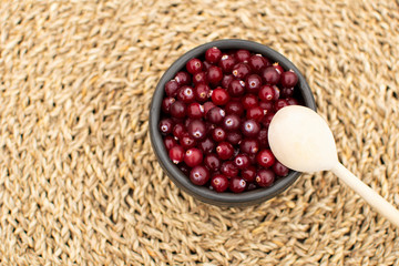 Winter dessert, top view at the bowl full of fresh cranberries at natural wicker background and wooden spoon above, authentic life