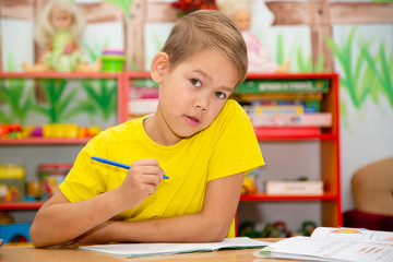 a boy in a yellow T-shirt performs an assignment at the table