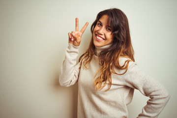 Young beautiful woman wearing winter sweater standing over white isolated background smiling looking to the camera showing fingers doing victory sign. Number two.