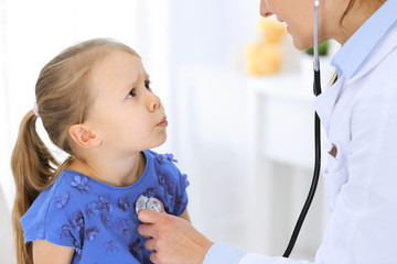 Doctor examining a little girl by stethoscope. Happy smiling child patient at usual medical inspection. Medicine and healthcare concepts