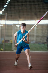Obraz premium Pole vault training in the sports stadium - young man running on the track holding a pole