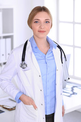 Young woman doctor at work in hospital looking at camera. Blue colored blouse of therapist looks good. Medicine and healthcare concept