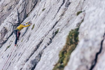 A climber climbing on a big rock wall. A mountaineer ascending a climbing route. Limestone climbing in the alps. Adventure extreme sport activity. Multi pitch climbing in huge alpine wall.