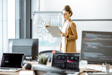 Young business woman preparing for a presentation, standing alone with documents near flipchart in...