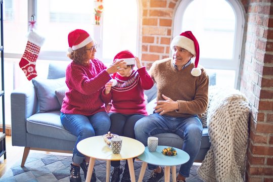 Beautiful family smiling happy and confident. Sitting on the sofa with smile on face wearing santa claus hat hugging around christmas decorations at home