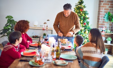 Beautiful family smiling happy and confident. One of them curving roasted turkey celebrating christmas at home